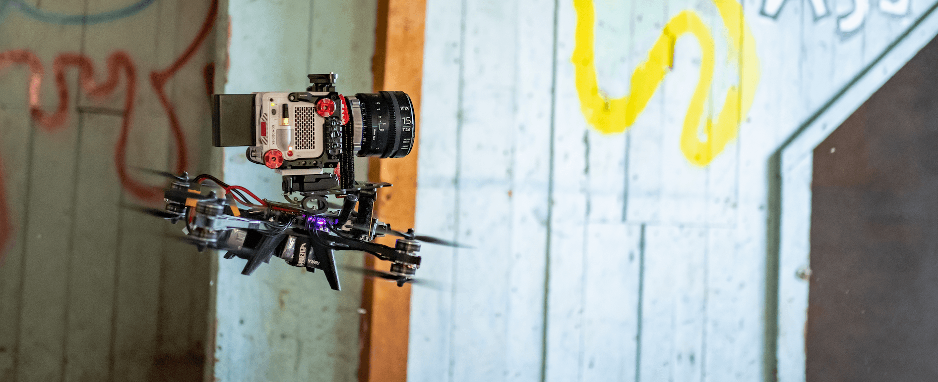 Cinema FPV drone carrying a RED camera, flying past a graffiti-covered wooden wall